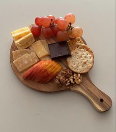 a wooden cutting board topped with cheese, crackers and fruit on top of it