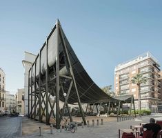 a large metal structure sitting on the side of a road next to tall buildings and palm trees