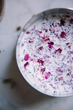 a bowl filled with white and red flowers on top of a marble counter next to nuts