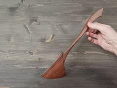 a hand holding a wooden paddle on top of a gray wood floor next to a wall