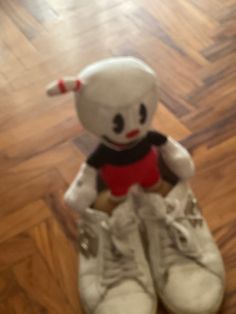 a white stuffed animal sitting on top of a pair of shoes in a room with hard wood flooring