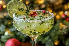 a margarita with lime and cranberries in front of a christmas tree