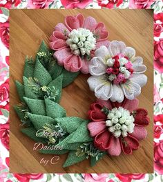 three different colored flowers are placed on a wooden surface in front of a pink and green wreath