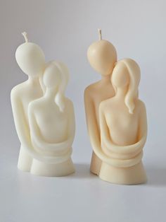 two candles sitting next to each other on a white surface with one candle in the shape of a woman holding a baby