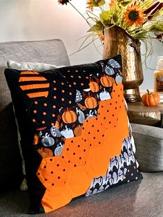 an orange and black pillow sitting on top of a couch next to a vase filled with flowers