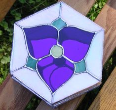 a purple and green stained glass box sitting on top of a wooden bench next to bushes