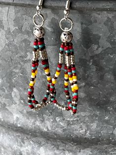 two pairs of colorful beaded earrings hanging from hooks on a stone wall with rock background