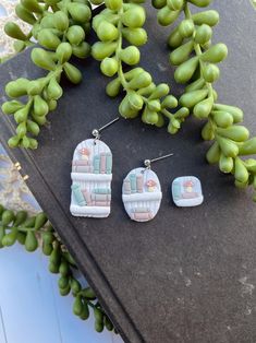 three pairs of earrings sitting on top of a table next to some green leaves and berries