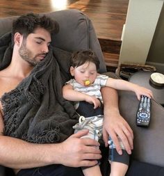 a man sitting in a chair holding a baby and a remote control next to him