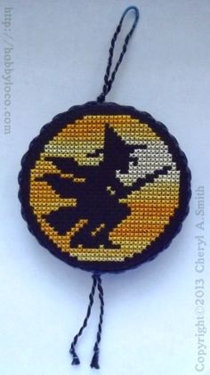 a cross stitch ornament with a black cat and yellow moon in the background