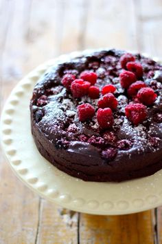 a chocolate cake topped with raspberries on top of a white plate and wooden table