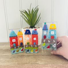 a hand is holding three small magnets with houses on them and a potted plant in the background