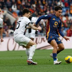 two men playing soccer on a field with people watching from the stands in the background