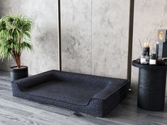 a plant and some candles on a wooden floor next to a black table with a blue cushion