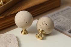 two white and gold knobs sitting on top of a piece of paper next to a wooden box