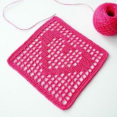 a pink crochet square next to a ball of yarn on a white surface