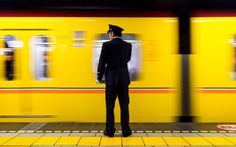 a train conductor standing on the platform in front of a yellow train with motion blur