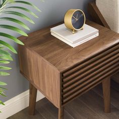 a small wooden table with a clock on it next to a chair and potted plant