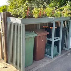 three bins with plants growing out of them on the side of a road in front of a fence