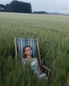 a woman is sitting in a lawn chair in the middle of a field with tall grass