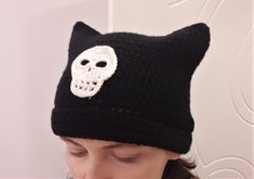 a woman wearing a black knitted hat with a white skull on the side and a cat's head