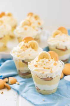 small desserts with banana slices and whipped cream in them on a blue napkin next to cookies