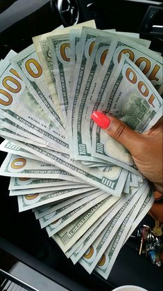 a woman's hand holding money in the back seat of a car on top of a pile of cash