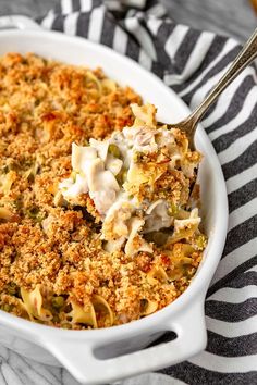 a white casserole dish filled with pasta and meat covered in cream sauce on a striped cloth