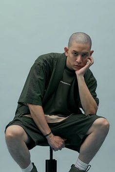 a young man sitting on top of a stool with his hand to his face while talking on a cell phone