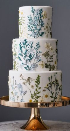 a three tiered cake decorated with flowers and leaves on a gold plated platter