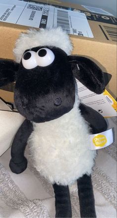 a black and white stuffed sheep sitting on top of a bed next to a box