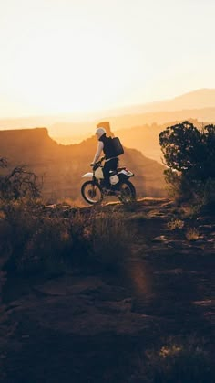 a person riding a dirt bike on top of a hill near the sun in the distance