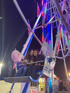 two women are sitting on a ferris wheel at an amusement park in the night time