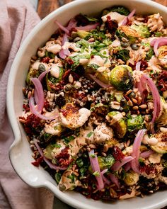 a salad with broccoli, cauliflower and red onions in a white bowl