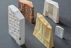 three models of buildings made out of paper on a gray surface with one building in the middle