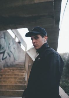 a young man wearing a black hat standing in front of graffiti covered wall and stairs