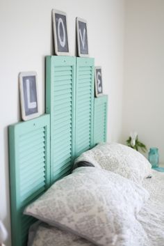 a bed with white sheets and blue shutters on the headboard is next to two framed pictures