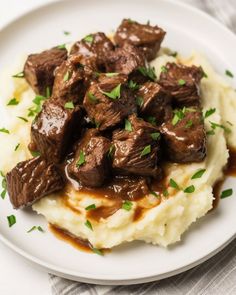 a white plate topped with mashed potatoes covered in beef and gravy on top of it