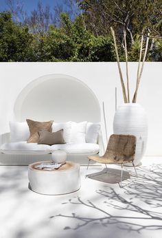 an outdoor living room with white furniture and trees in the backgroung area