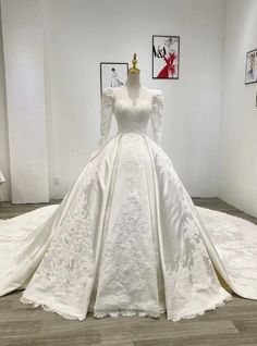 a white wedding dress on display in a room with pictures and other items around it