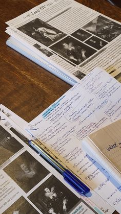 an open notebook sitting on top of a wooden table next to papers and pencils