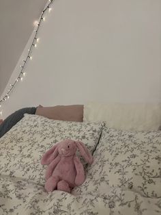 a person laying in bed with a pink stuffed animal on it's side and lights strung above the bed