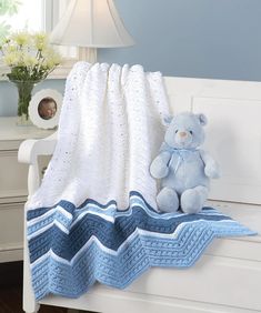 a blue teddy bear sitting on top of a white bench next to a blanket and flowers