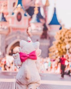 a white stuffed animal with a pink bow on it's back in front of a castle