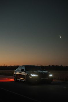 a car driving down the road at night with the moon in the sky behind it