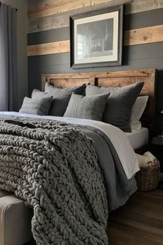 a bed with gray blankets and pillows in a bedroom next to a window, framed by wood planks