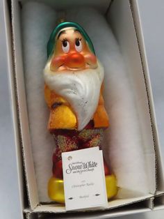 an orange and green gnome figurine in a white box with a tag on it