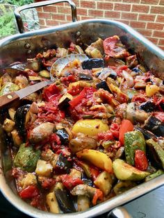 a large pan filled with lots of food on top of a metal table next to a brick wall