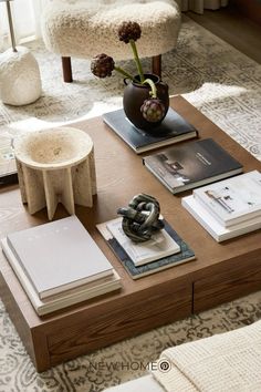 a coffee table with books, magazines and a vase on it in a living room