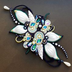 a brooch that is laying down on a brown surface with white flowers and green leaves